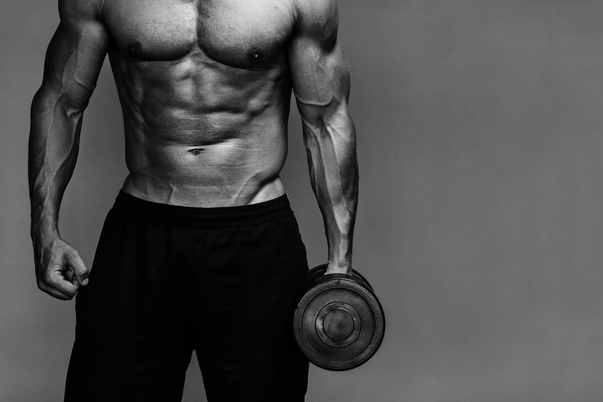 Muscular man holding a dumbbell, shown in grayscale.