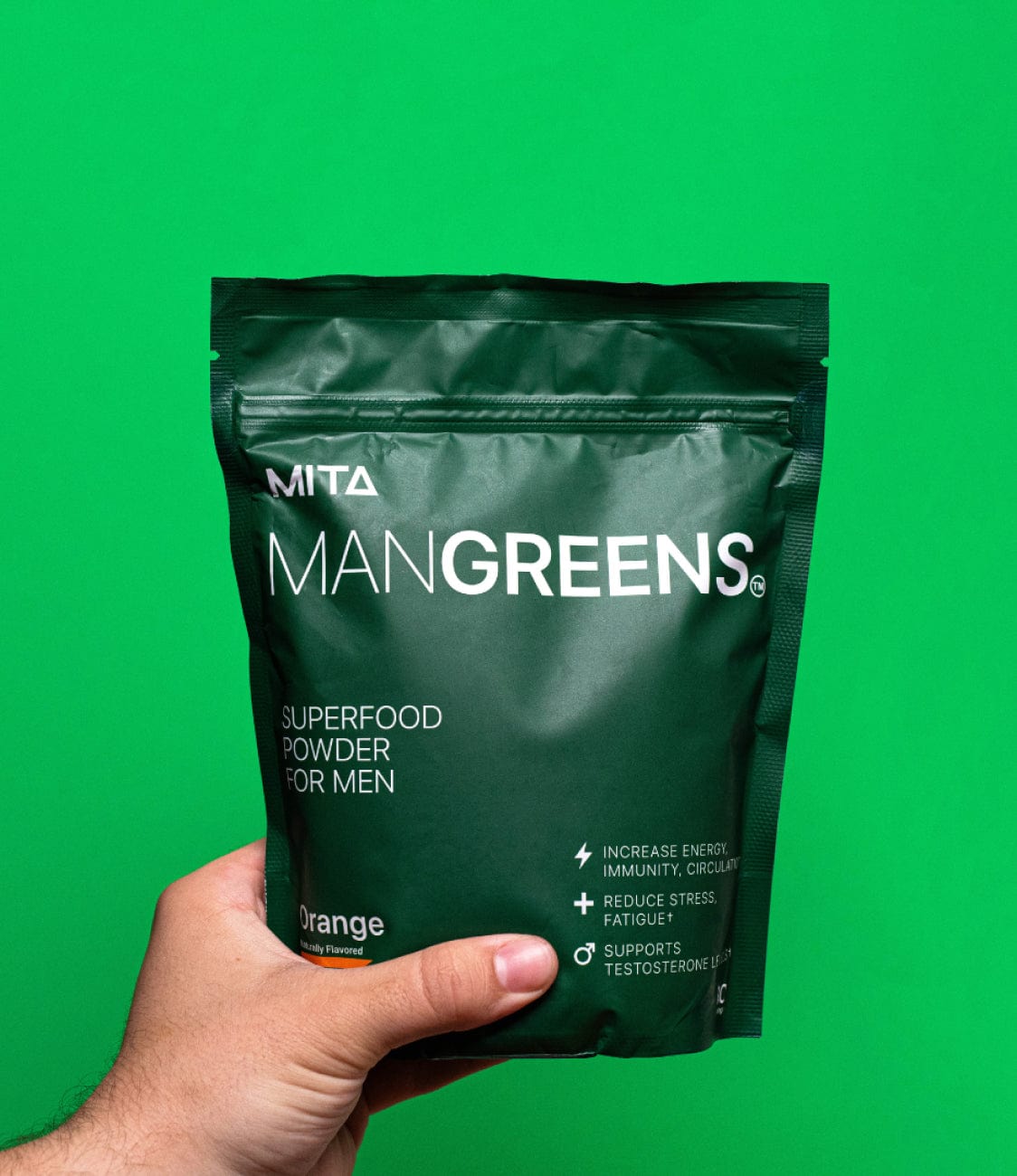 Hand holding a green bag of ManGreens superfood powder against a green background.