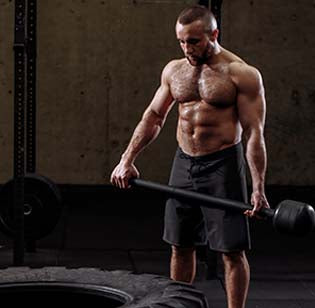 A man in gym shorts holding a sledgehammer next to a large tire.