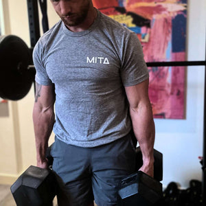 Man in gym holding two heavy dumbbells in front of a colorful abstract artwork.