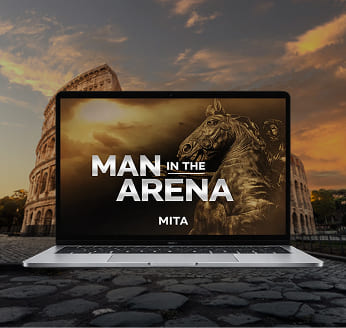 A laptop on a cobblestone surface displays 'MAN IN THE ARENA' with the Roman Colosseum in the background.