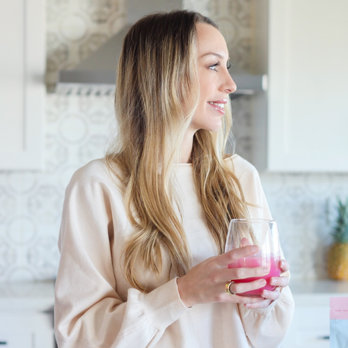 Woman holding a pink drink in a kitchen, looking to the side.