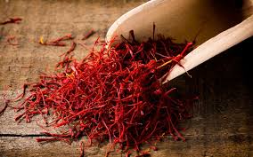 Red saffron threads spilled from a small wooden scoop on a wooden surface.