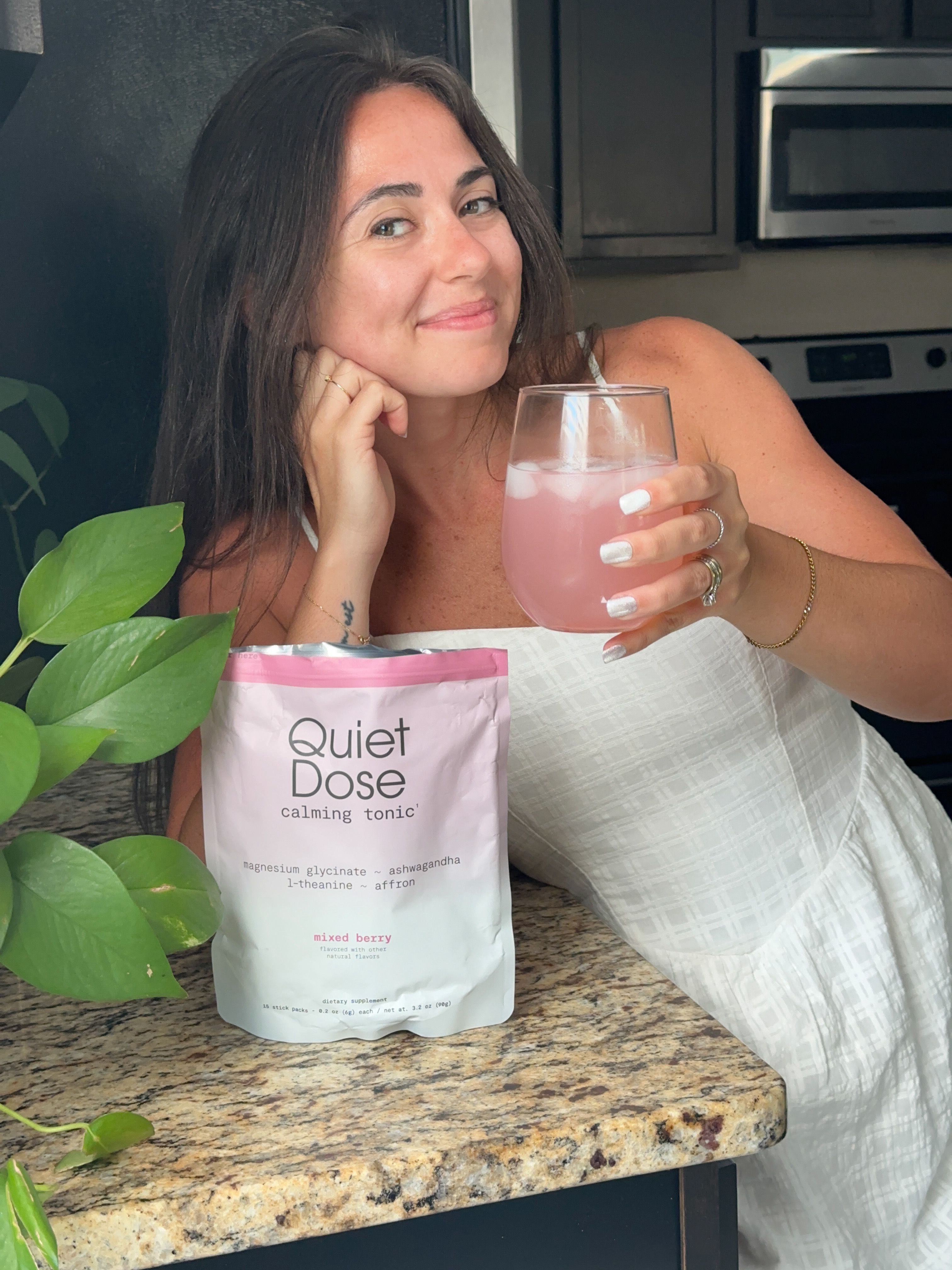 Person smiling, holding a drink, next to a packet labeled 'Quiet Dose calming tonic.'