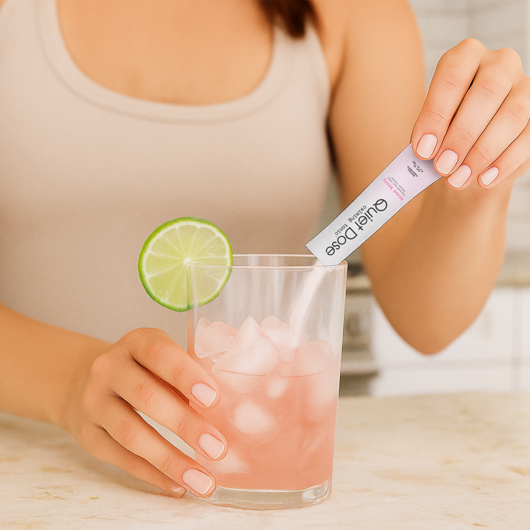 Person adding a supplement to a glass of pink drink with lime and ice.
