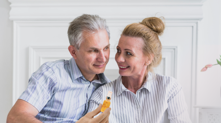 A couple smiling at each other, holding a small bottle.