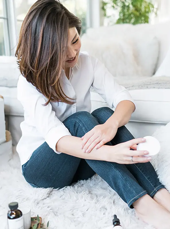Person sitting on a fuzzy rug, holding a container, surrounded by skincare products.
