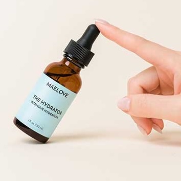 A hand touches the dropper top of a tilted bottle of Maelove The Hydrator serum.