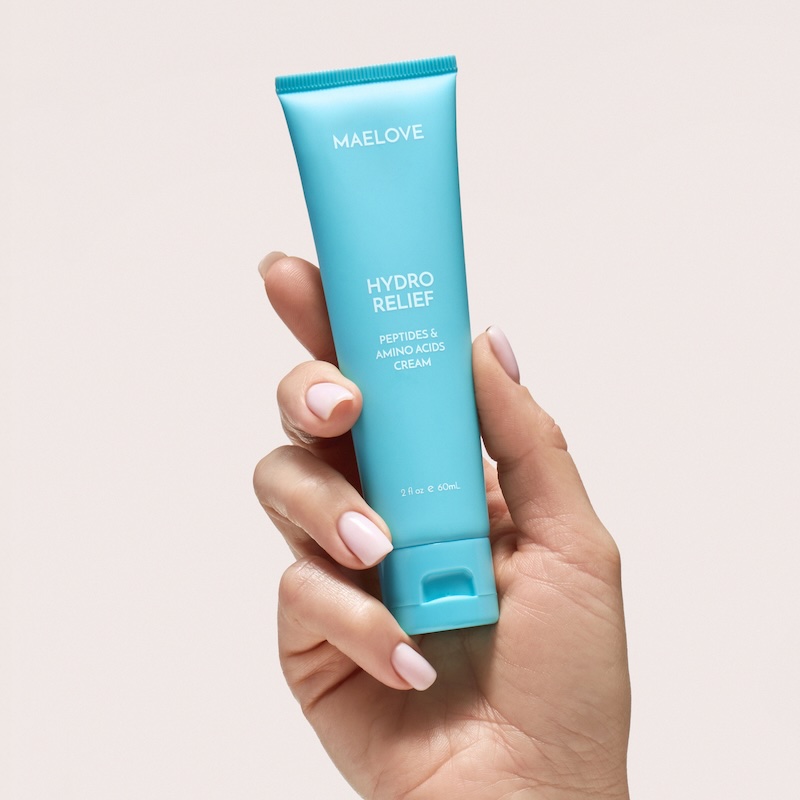A hand with a light pink manicure holds a light blue tube of Maelove Hydro Relief cream.