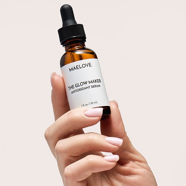 A hand with a light pink manicure holding a bottle of Maelove's The Glow Maker antioxidant serum.