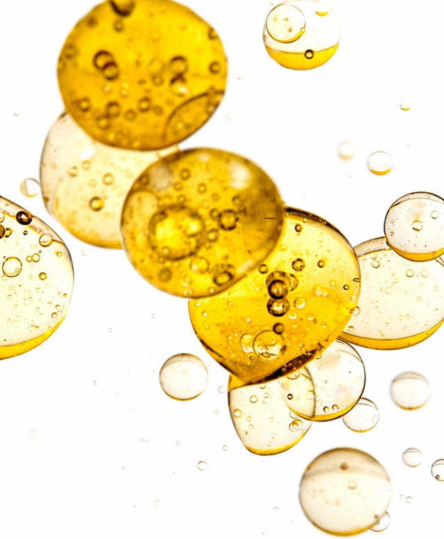 A close-up, abstract image of golden yellow oil bubbles suspended in a clear liquid against a white background.