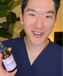 A smiling man in blue scrubs holds up a small brown glass bottle with a dropper.