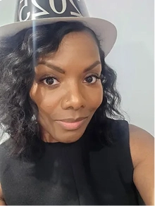 A woman with dark curly hair and a nose piercing wearing a black top and a party hat.
