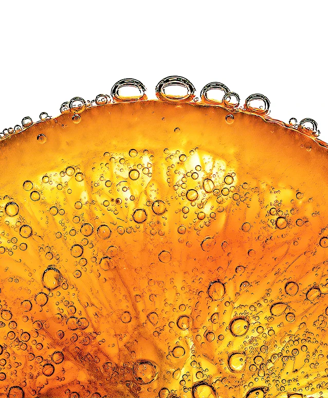 A close-up of a slice of orange covered in carbonation bubbles against a stark white background.