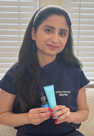 Person holding skincare products, wearing a navy shirt with a name embroidered.