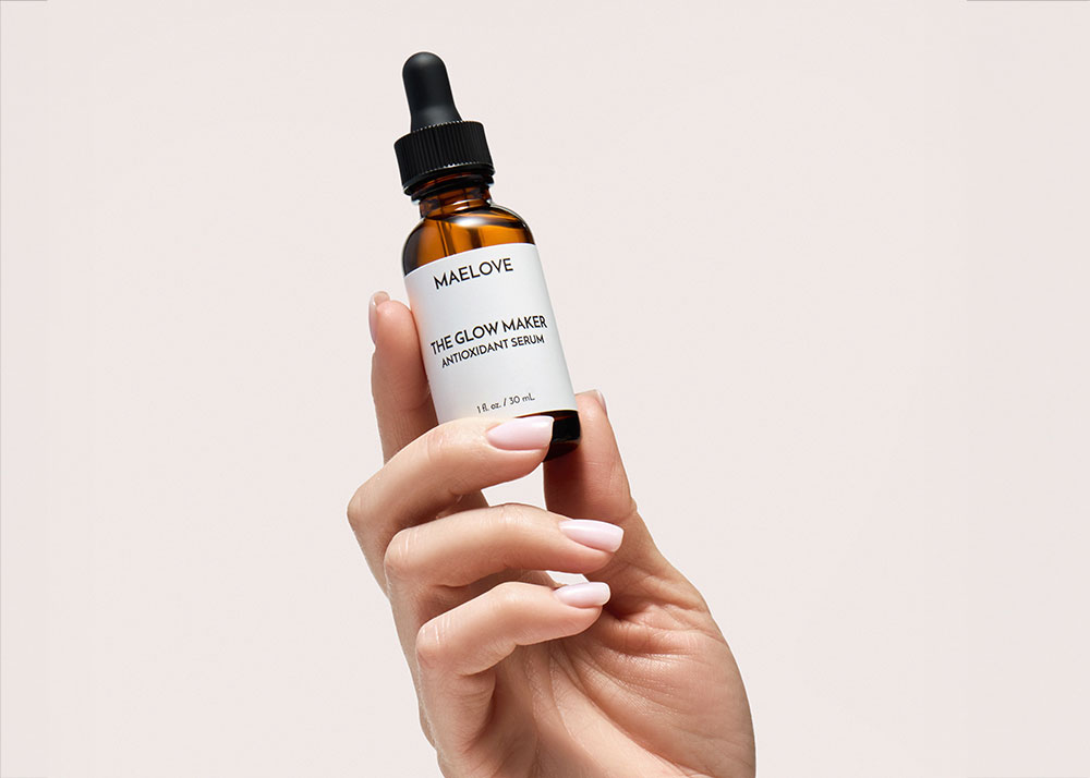 A hand with a light pink manicure holding a bottle of Maelove's The Glow Maker antioxidant serum.