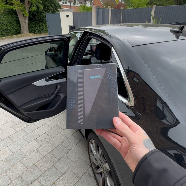 Hand holding a black package labeled 'digidash' near an open car door.