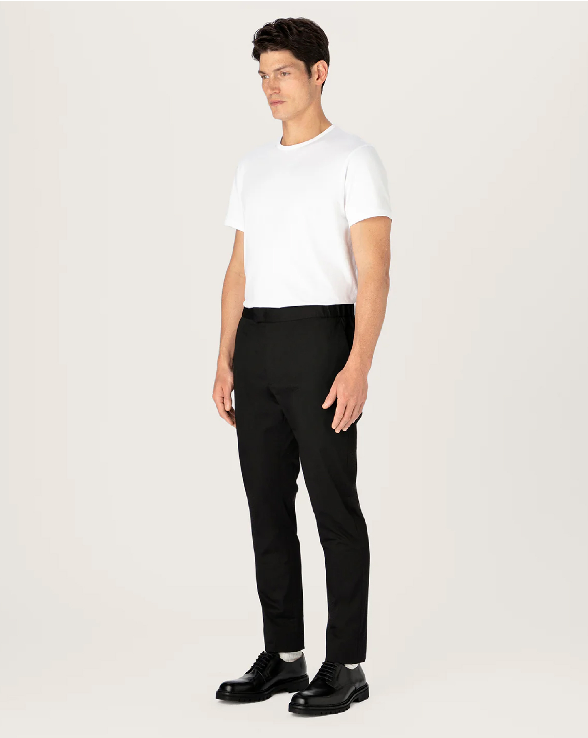 Man in white shirt and black pants standing on a light background.
