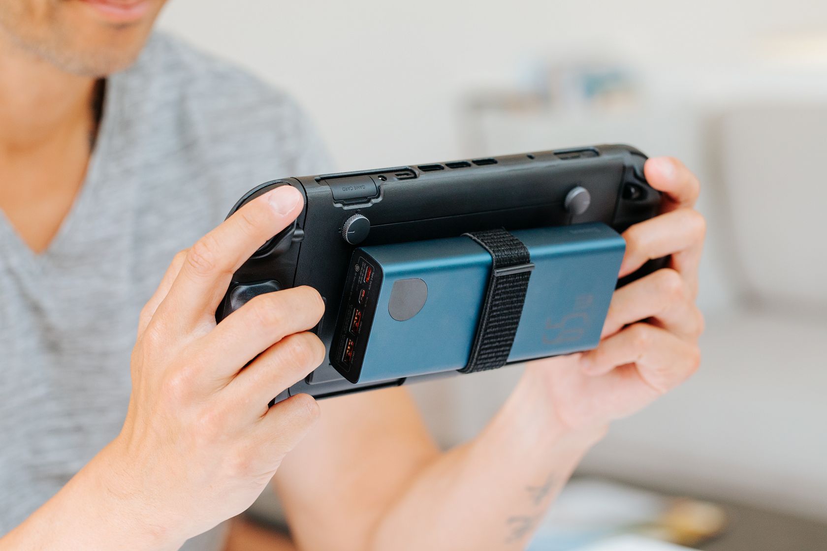 A person holding a handheld gaming console with a blue power bank strapped to the back.