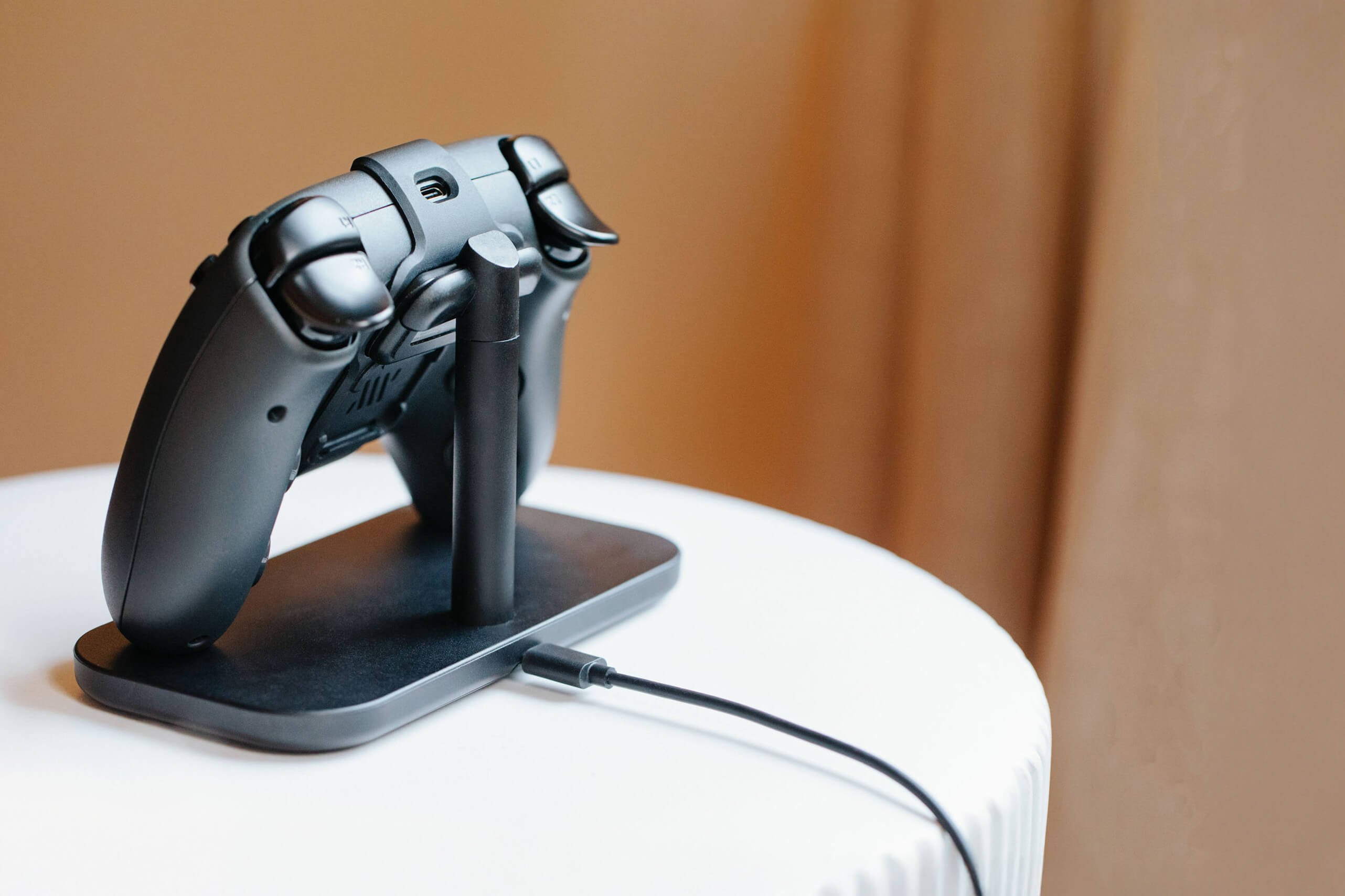 A black video game controller resting on a charging stand on a white table.