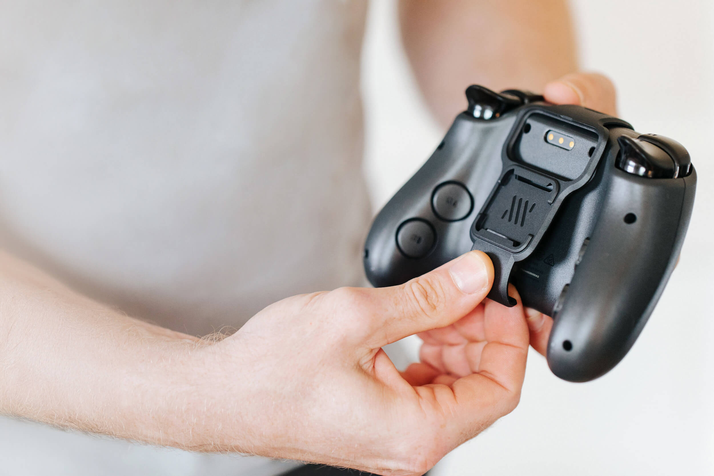 A close-up of a person's hands attaching a charging pack to the back of a black game controller.