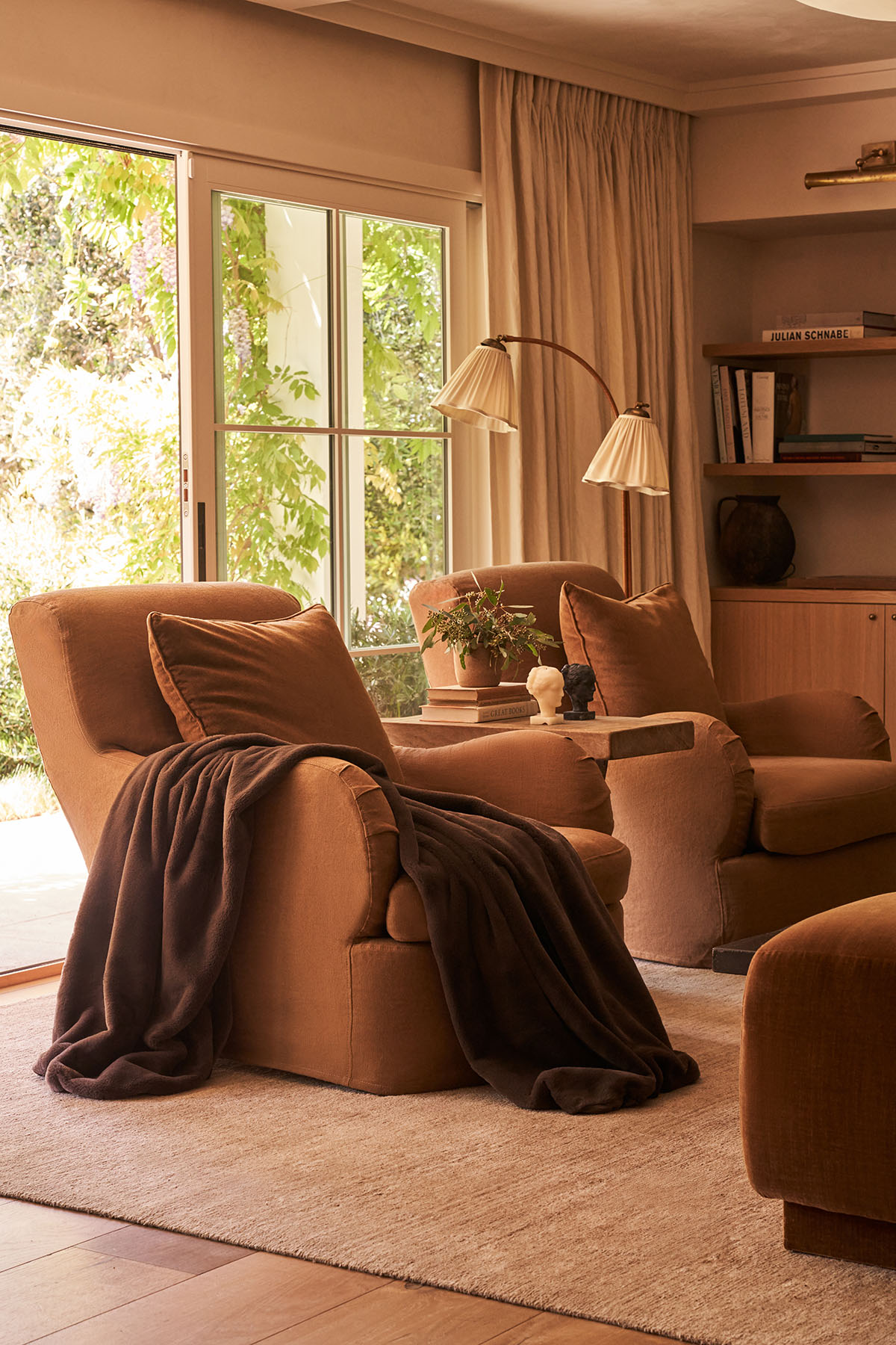 Cozy seating area with armchairs, throw blanket, and plants by a large window.