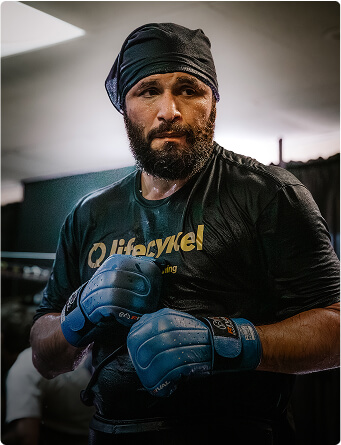 Man in boxing gloves and headscarf, wearing a black shirt, standing indoors.