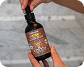 A brown bottle of oil with a dropper sits on a marble bathroom counter next to a faucet.