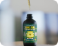 A drop of liquid falls from a dropper into a dark bottle with a green and yellow label.
