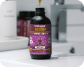 A dropper dispenses a golden liquid into a dark bottle with a purple label on a bathroom counter.