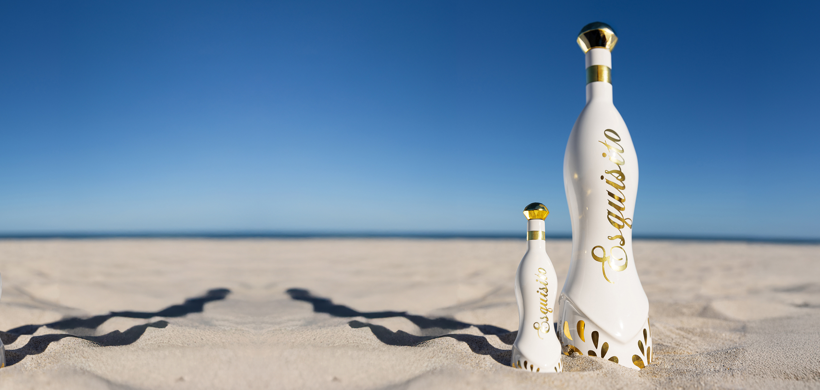 Two elegant bottles with gold accents on a sandy beach.