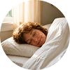 A woman with curly hair sleeping peacefully in bed under a white comforter.