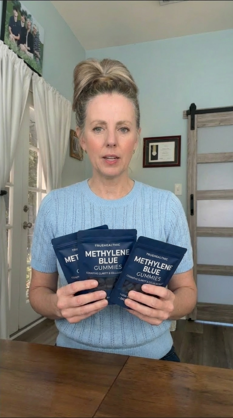 A woman in a blue sweater holds up three pouches of Methylene Blue Gummies.