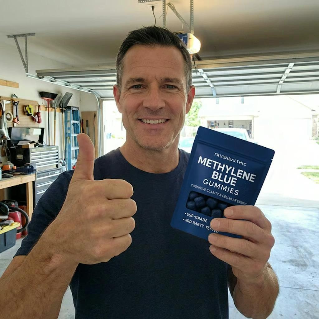 A smiling man in a garage gives a thumbs-up while holding a pouch of Methylene Blue Gummies.