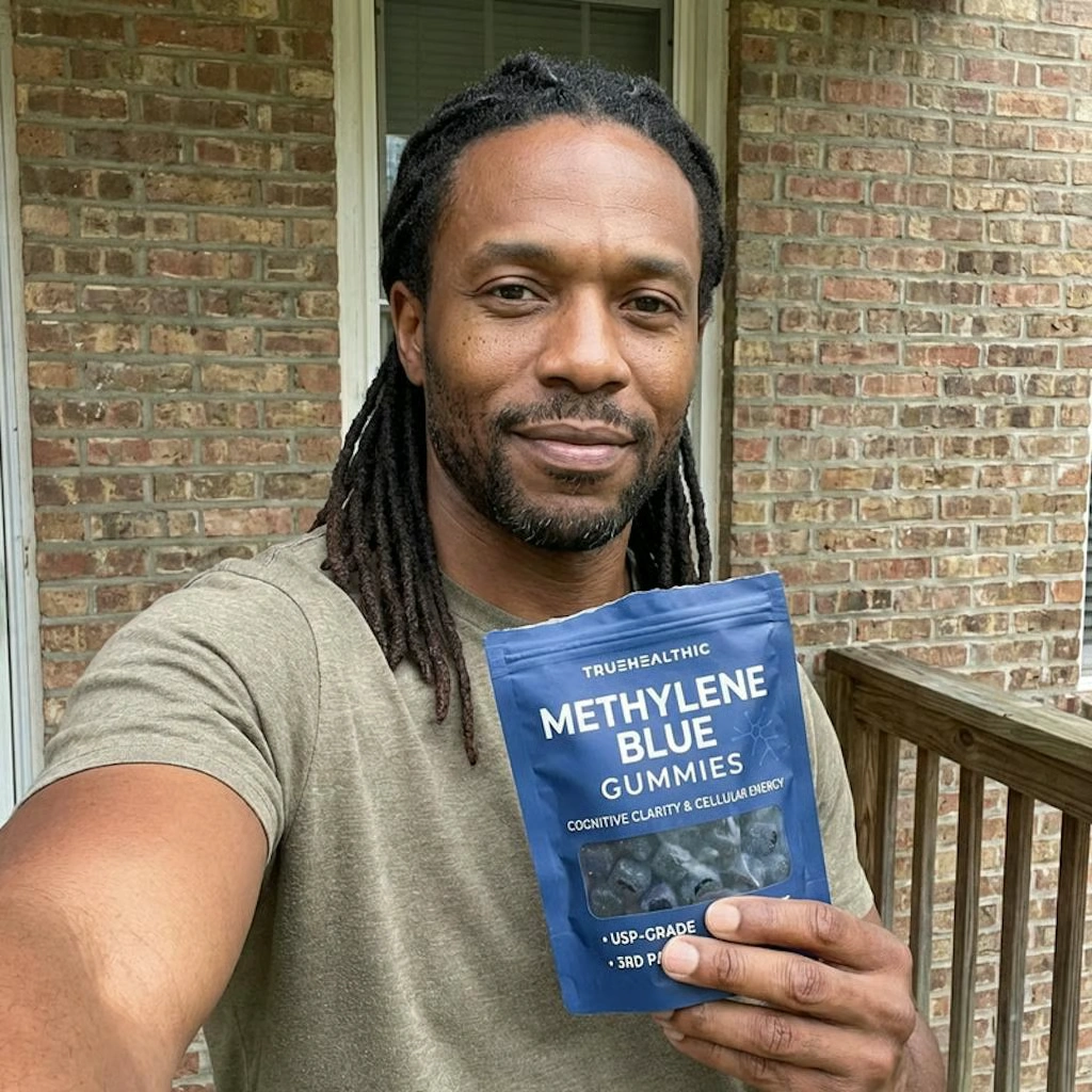 A man with dreadlocks holds a pouch of Truehealthic Methylene Blue Gummies in front of a brick wall.