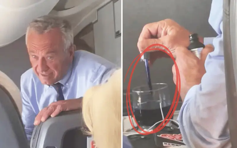 Man in blue shirt on airplane, stirring drink with pen.
