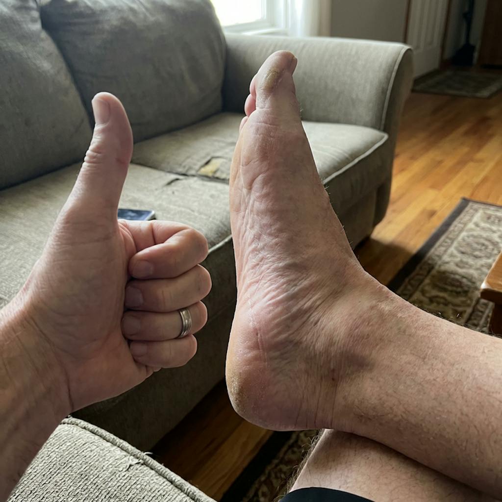 A person gives a thumbs-up sign with their hand next to their bare foot.