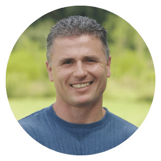 Smiling person in a blue shirt with a blurred green background.