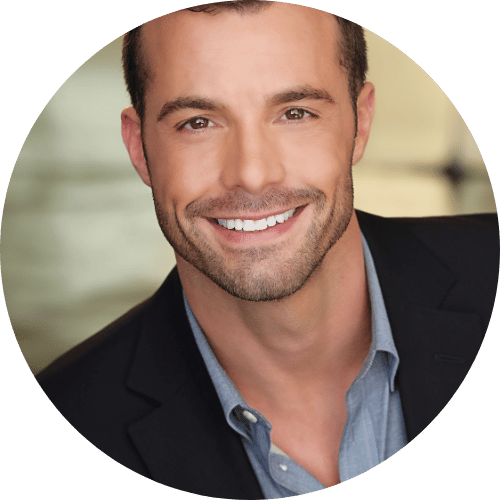 Smiling man in a suit jacket with a blurred background.