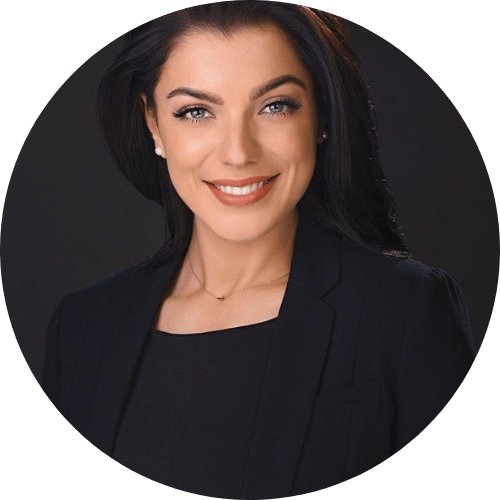 Smiling person in a black blazer against a dark background.