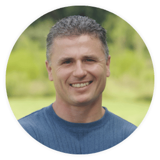 Smiling person in a blue shirt with a blurred green background.