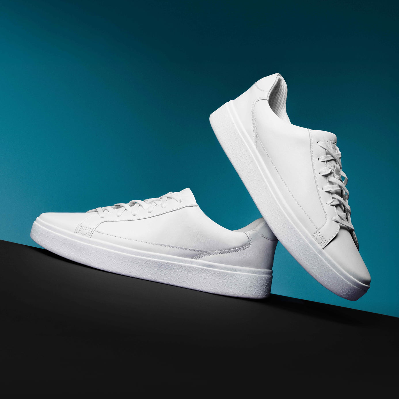 Two white sneakers on a black and teal background.
