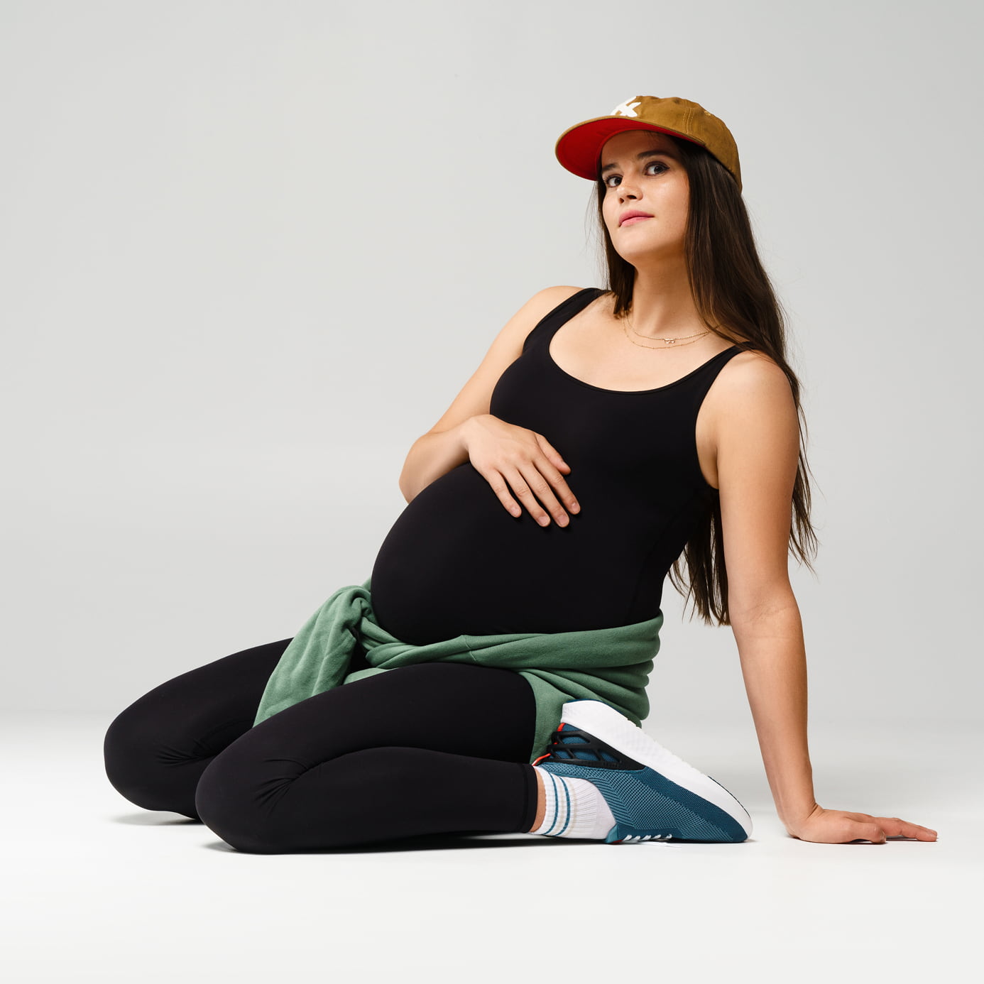 Pregnant woman in black outfit and cap sitting on the floor.