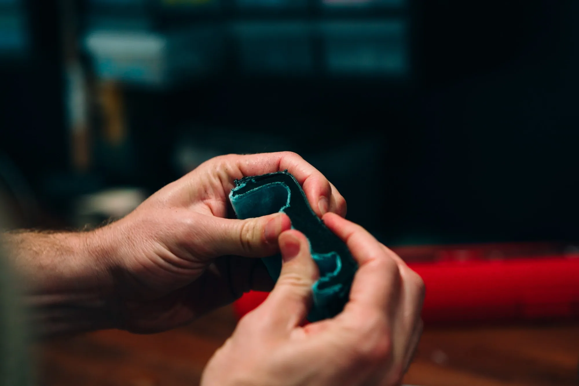 Two hands working a piece of teal foam at a workbench