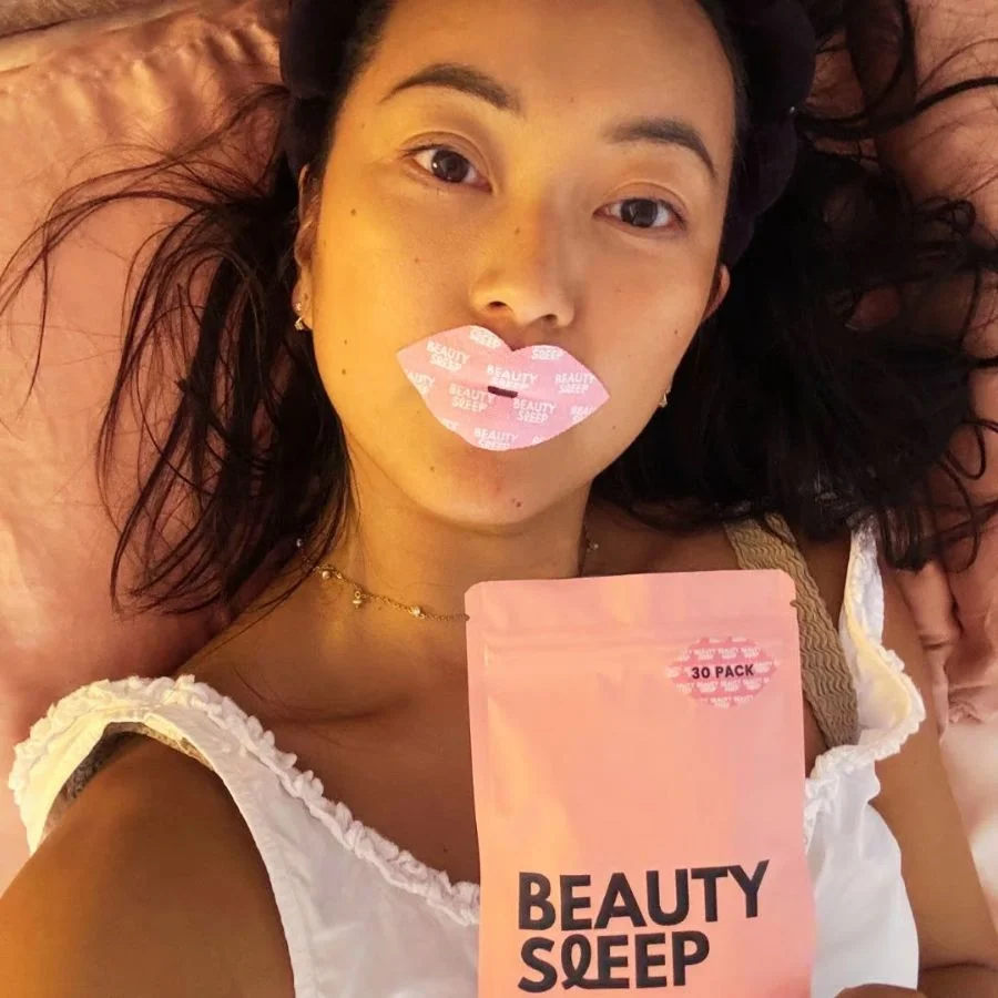 Person lying down with a lip mask and holding a 'Beauty Sleep' package.