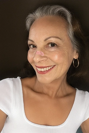 Smiling woman with hoop earrings and a white top against a dark background.
