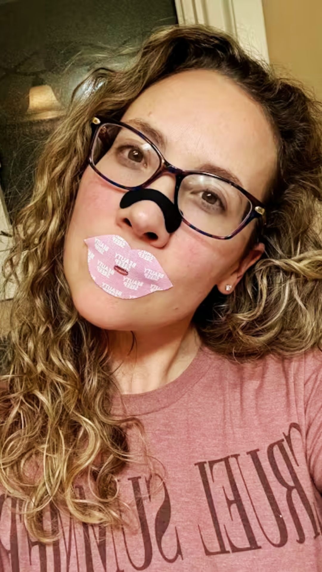 A woman wearing glasses, a black nose strip, and a pink, lip-shaped mouth strip.