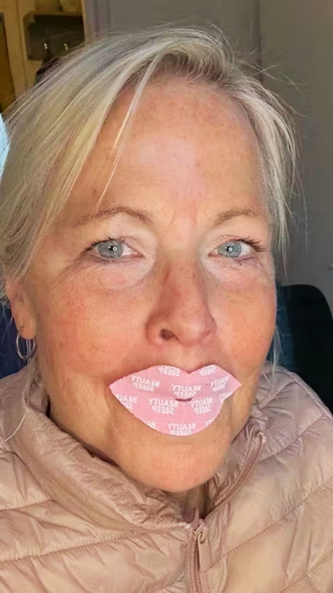 A close-up of a woman with a pink, lip-shaped patch with text on it over her mouth.