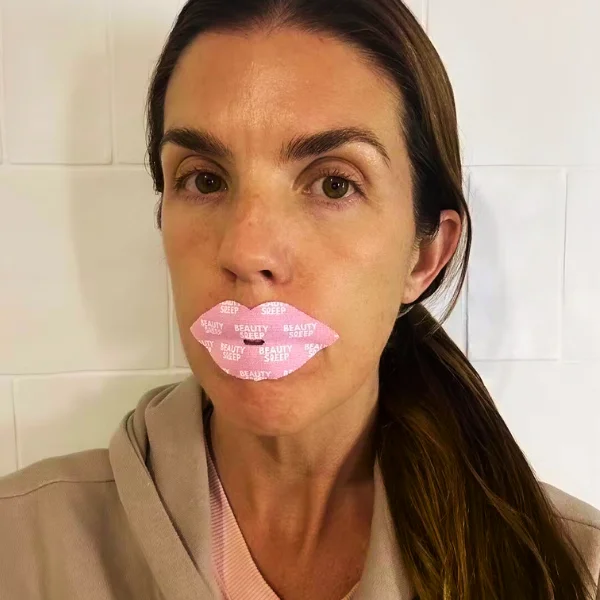 Person with pink lip-shaped patch on mouth, wearing a beige hoodie.