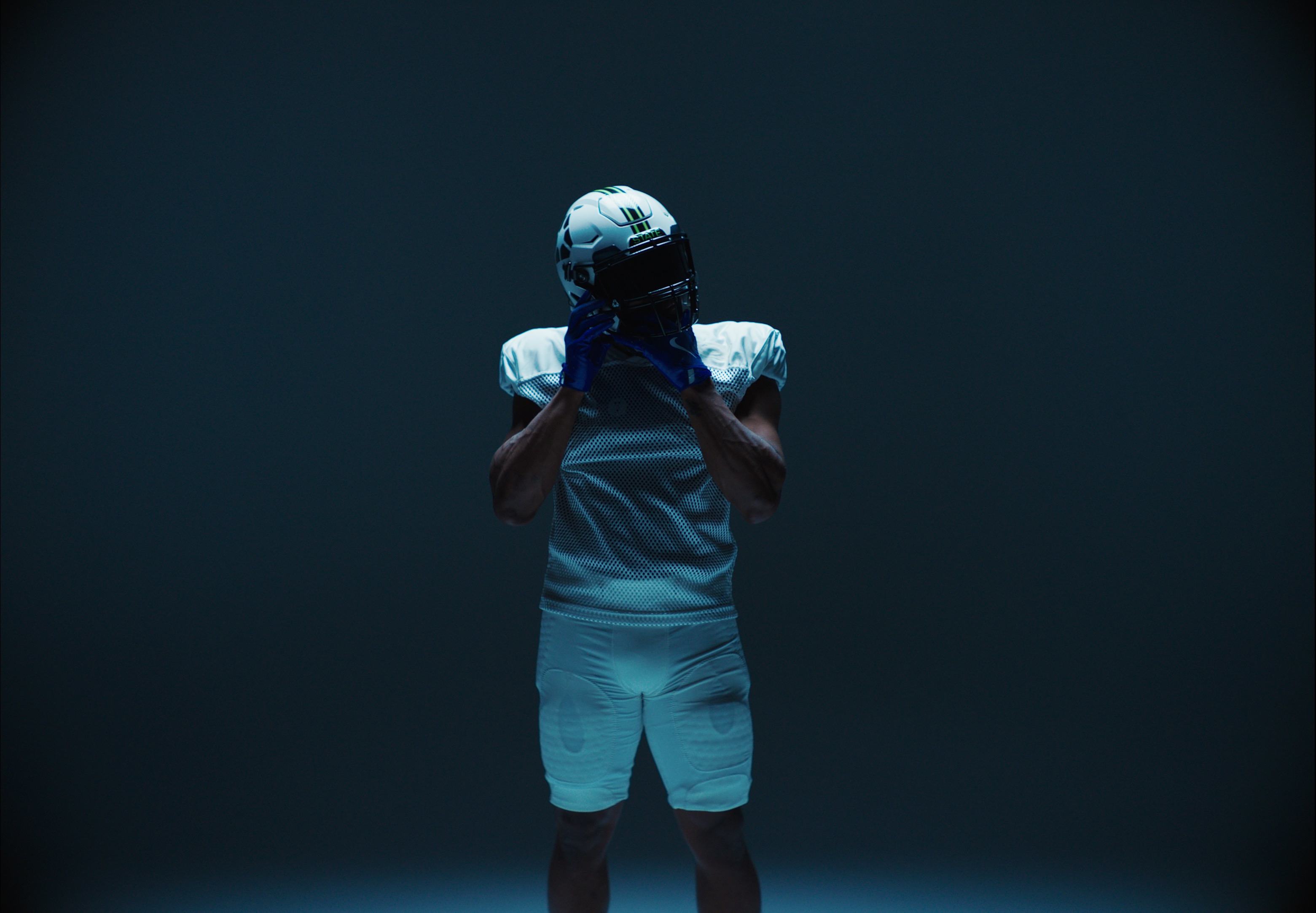 Football player in white uniform and helmet adjusting face mask.